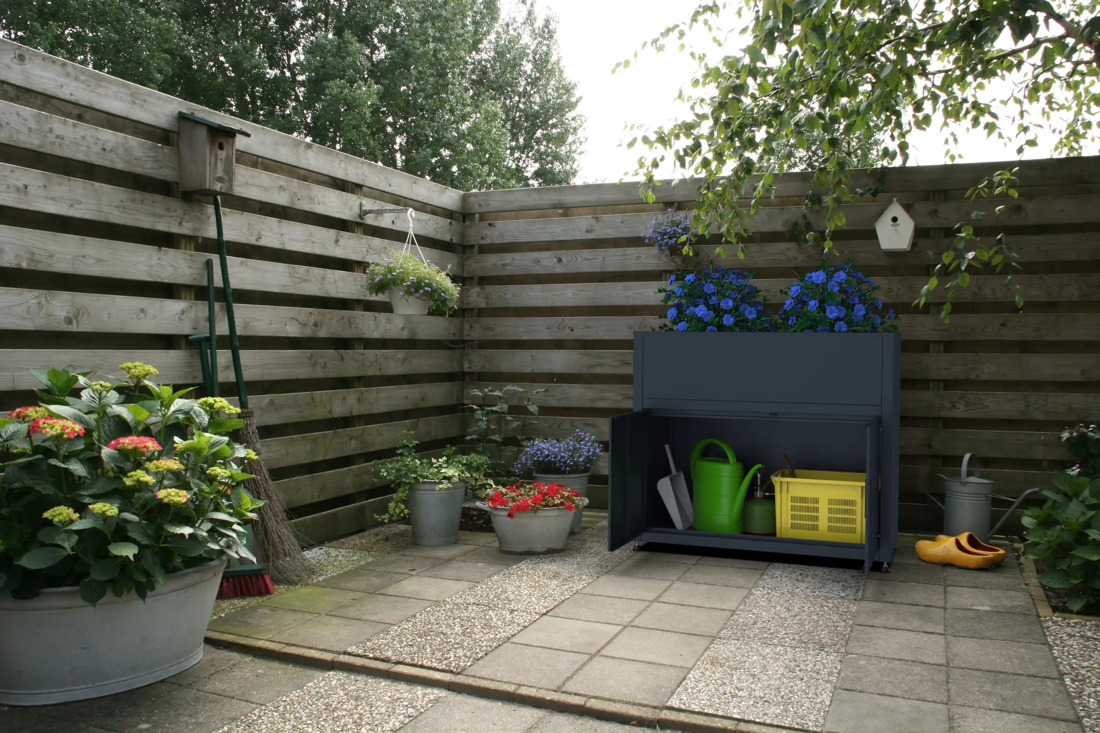 Geöffneter Gartenschrank unter dem Hochbeet zur Aufbewahrung von Gießkanne und Werkzeug.