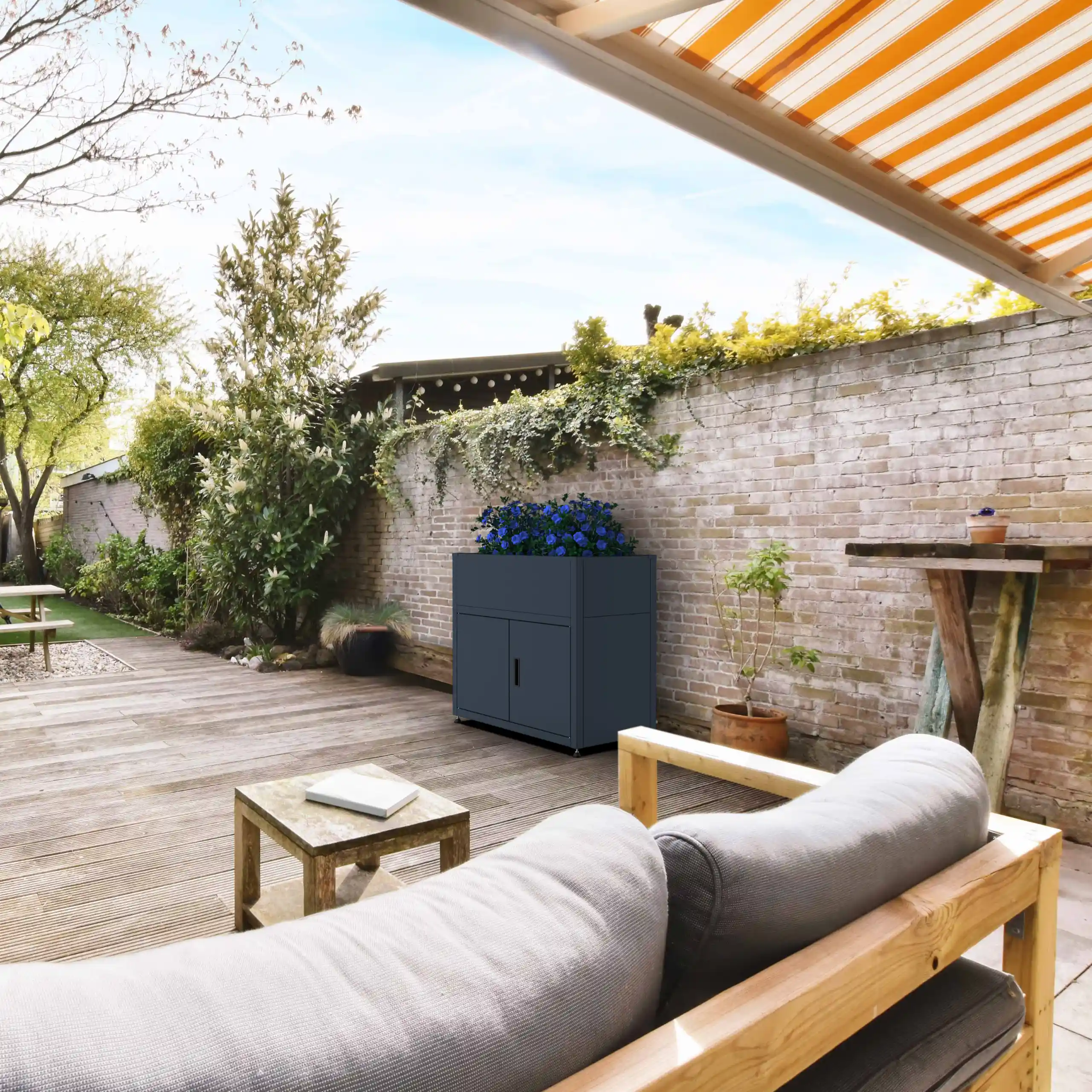 Anthrazitfarbener Pflanzkasten mit blauen Blumen als Dekoration auf einer sonnigen Holzterrasse.